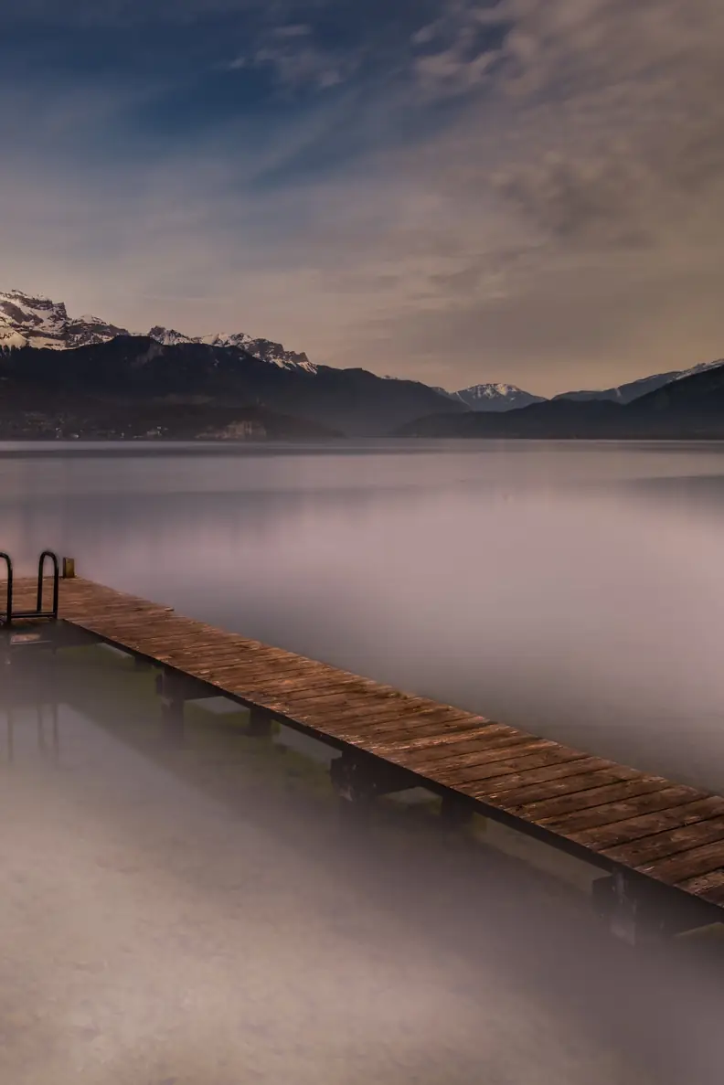Ponton en bois sur le lac d'Annecy au crépuscule, avec les montagnes enneigées en arrière-plan